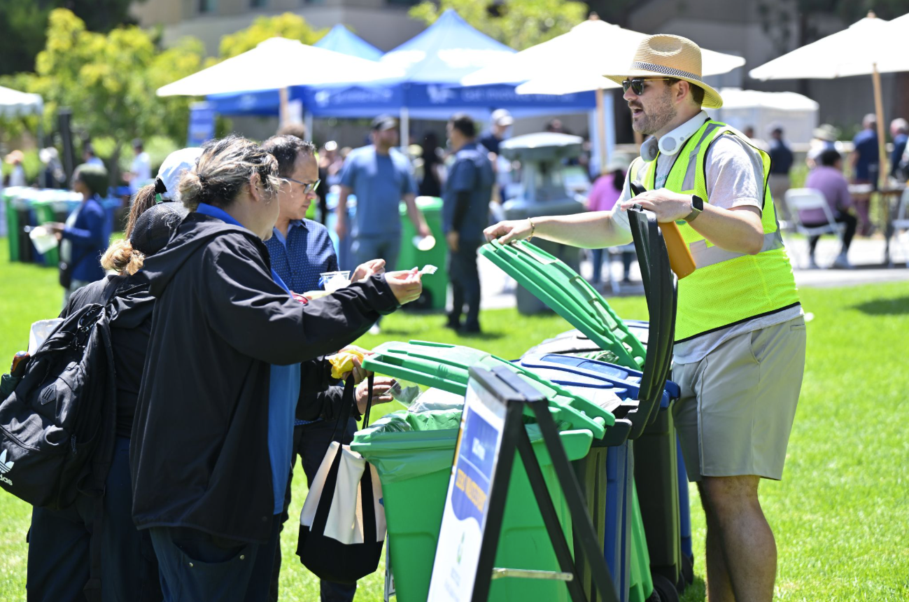 A Trash Talker volunteer in a safety vest helping picnic attendees sort their waste into compost, recycling, and landfill bins